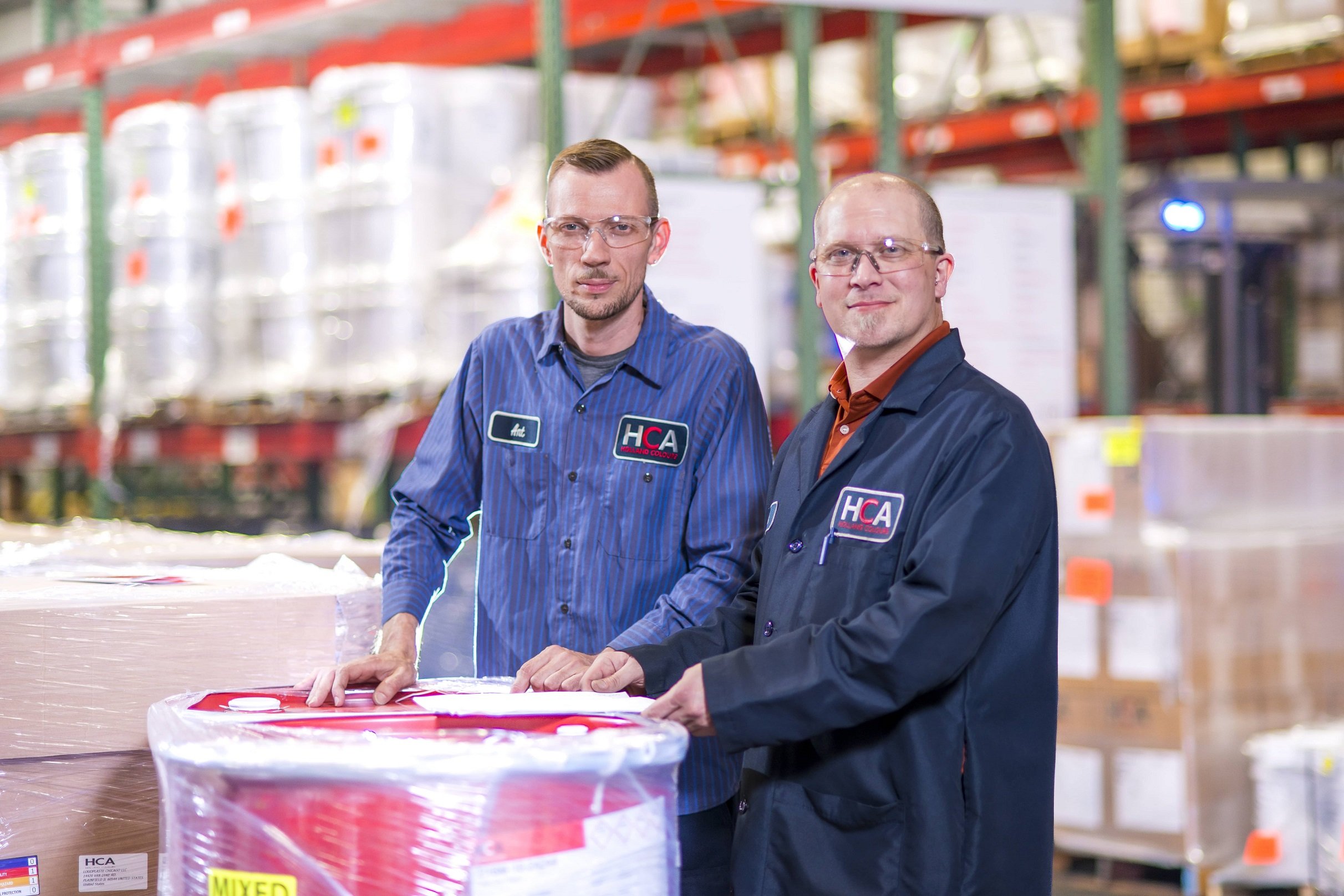 two Holland colours production employees standing next to a red paint barrel